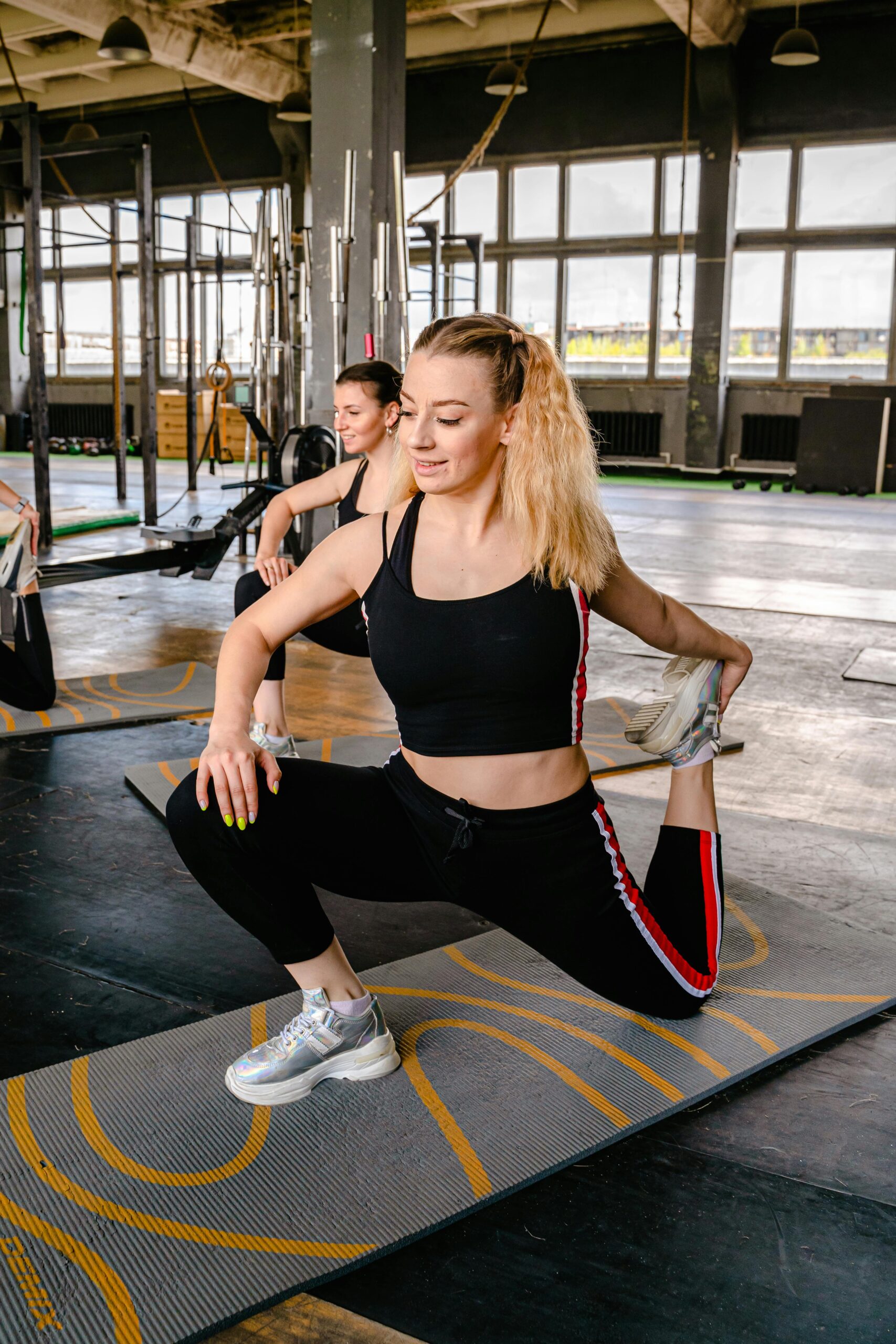 Two women in active wear stretching on yoga mats in a gym, promoting health and wellness.