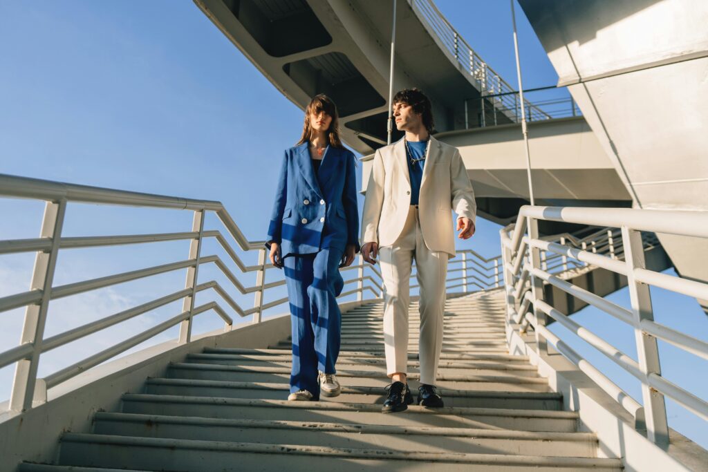 Stylish man and woman in blue and white suits walking down an industrial staircase.